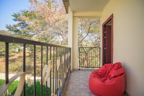 A balcony with a red bean bag chair, a metal railing, and a view of trees and a building in the background. - Beautiful 2-bedroom apartment in gated and secure community (Lusaka)