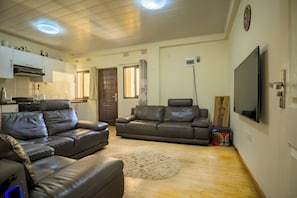 A living room with two leather sofas, a flat-screen TV, a fireplace, and a kitchen area with cabinets and a stove. - Beautiful 2-bedroom apartment in gated and secure community (Lusaka)