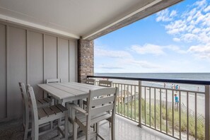 A balcony with a table and chairs, overlooking a beach with people in the distance. - 3 Bedroom Oceanfront: Stargazing from the 2nd Flr (Pawleys Island)