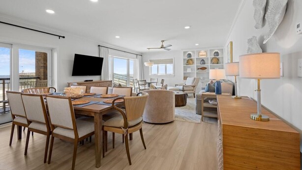 A modern living room with a dining area, a flat-screen TV, and a balcony with a view. - 3 Bedroom Oceanfront: Stargazing from the 2nd Flr (Pawleys Island)