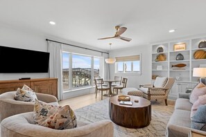 A modern living room with a flat-screen TV, comfortable seating, a dining area, and a view of a bridge. - 3 Bedroom Oceanfront: Stargazing from the 2nd Flr (Pawleys Island)
