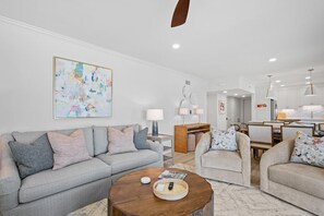 A modern living room with a grey sofa, a round coffee table, and a dining area with chairs and a table. - 3 Bedroom Oceanfront: Stargazing from the 2nd Flr (Pawleys Island)