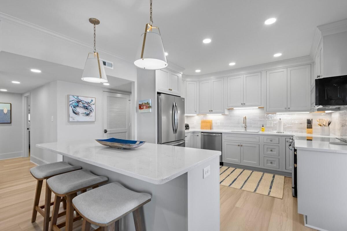 A modern kitchen with white cabinetry, a central island with bar stools, stainless steel appliances, and pendant lighting.