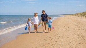 Una famiglia che cammina lungo una spiaggia sabbiosa, con l'oceano sullo sfondo.