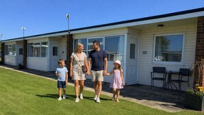 Una famiglia che cammina di fronte a una casa mobile con garage, un patio con sedie e un piccolo giardino.