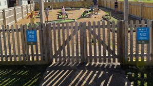 Un cartello di legno per ASiS Crazy Golf con una recinzione di legno sullo sfondo.