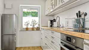 A modern kitchen with white cabinetry, stainless steel appliances, and a wooden countertop. - "Poeler Küstenkoje" Vacation Rental for 4 People (Insel Poel / OT Kirchdorf)