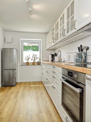 A modern kitchen with white cabinetry, stainless steel appliances, and a wooden countertop. - "Poeler Küstenkoje" Vacation Rental for 4 People (Insel Poel / OT Kirchdorf)