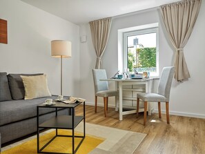 A modern living room with a sofa, a coffee table, a dining table with chairs, and a window with curtains. - "Poeler Küstenkoje" Vacation Rental for 4 People (Insel Poel / OT Kirchdorf)