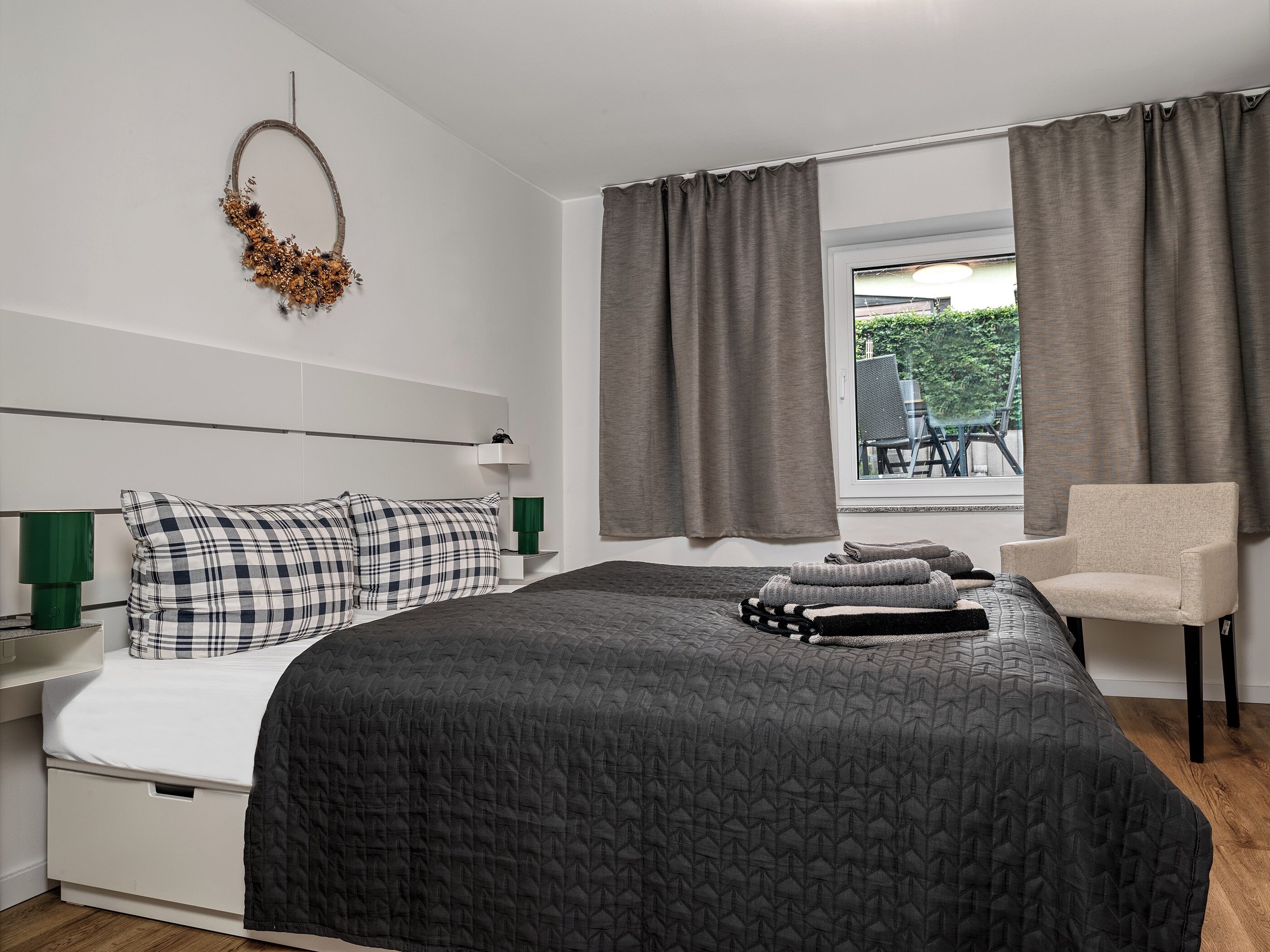 Een slaapkamer met een bed, een stoel, een raam met gordijnen en een wandlamp.