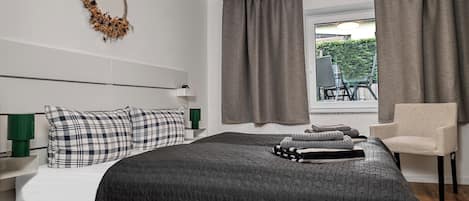 Un dormitorio con cama, una silla, una ventana con cortinas e iluminación montada en la pared.
