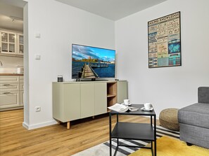 A modern living room with a flat-screen TV, a dining table with chairs, a sofa, and a poster on the wall. - "Poeler Küstenkoje" Vacation Rental for 4 People (Insel Poel / OT Kirchdorf)