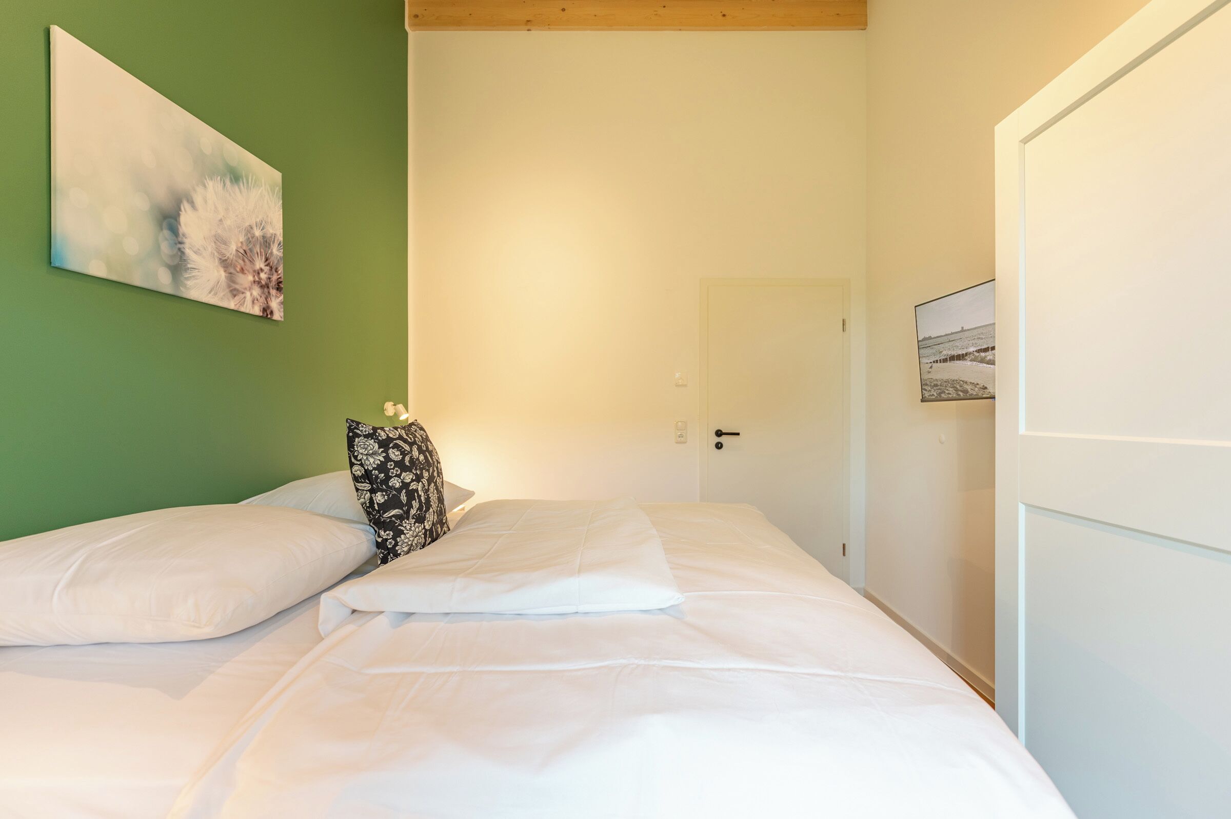 Un dormitorio con cama, almohadas, un cuadro en la pared y una puerta.