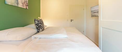 Quarto com cama, almofadas, um quadro na parede e uma porta.