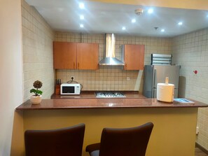 A kitchen with a microwave, stove, and refrigerator. There are two chairs and a small plant on the counter. - Bright 2-bedroom apartment with AC in fantastic Dubai location (Dubai)