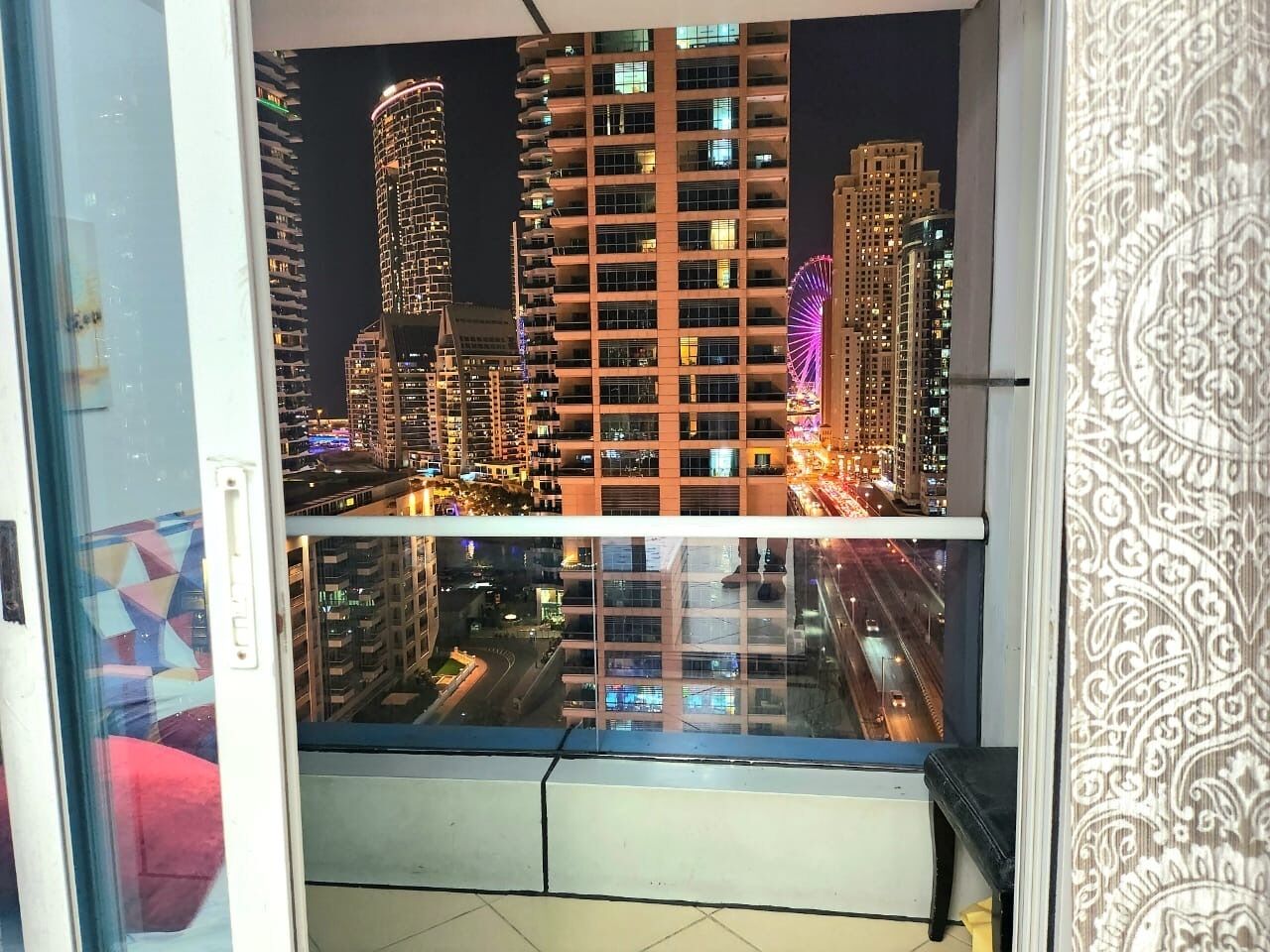 Vista des d'un balcó sobre una ciutat amb edificis alts i una noria.