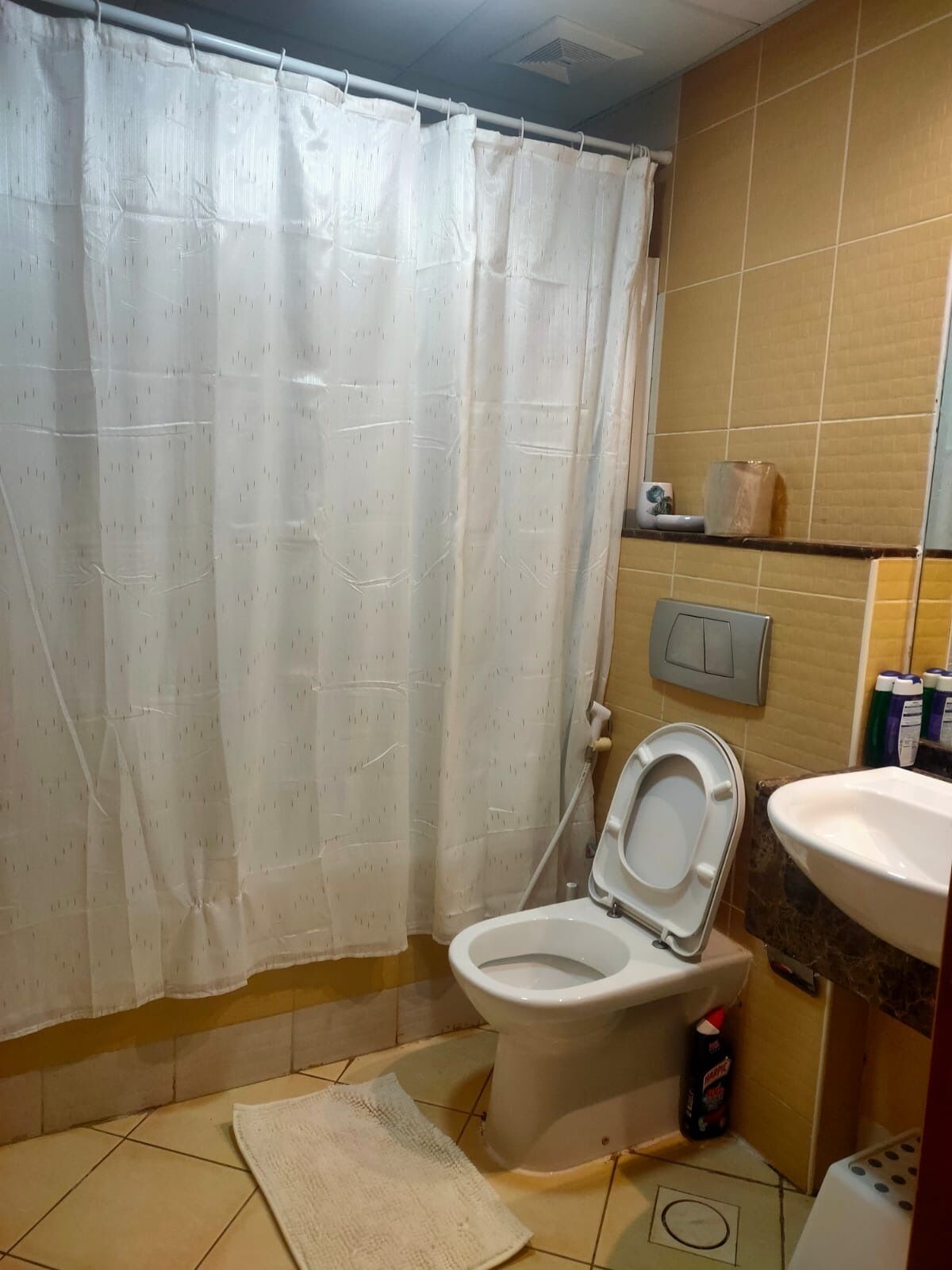 A bathroom with a toilet, a shower curtain, a sink, and a mop bucket.