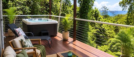 A deck with a sofa, a hot tub, and potted plants.