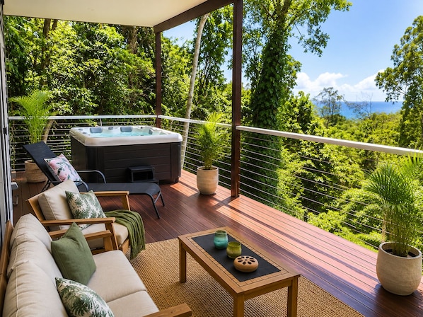 A deck with a sofa, a hot tub, and potted plants.