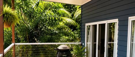A wooden deck with a ceiling fan, outdoor furniture, and a view of lush greenery.