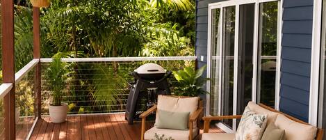 A covered outdoor deck with wooden furniture, a ceiling fan, and a view of lush greenery.