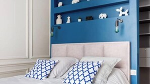 Ein Schlafzimmer mit einem Bett, zwei Kissen, einer blauen Wand und einem Regal mit Dekoration.