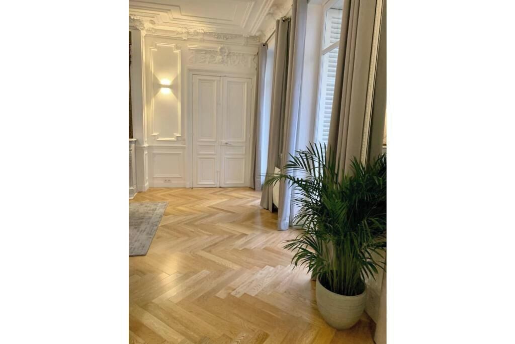 Un couloir avec un plancher en bois, des portes blanches et une plante en pot.
