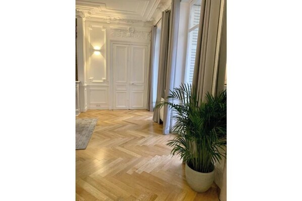 A hallway with a wooden floor, white doors, and a potted plant. - Very spacious, recently renovated apartment near Madeleine (Île-de-France)