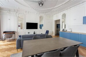 A room with a dining table, a sofa, a TV, and a kitchen area. - Very spacious, recently renovated apartment near Madeleine (Île-de-France)