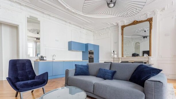 Ein modernes Wohnzimmer mit grauem Sofa, blauem Sessel und einem Glastisch.