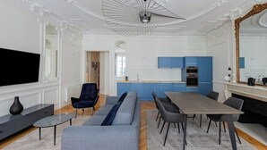 Ein modernes Wohnzimmer mit einer Couch, einem Esstisch und Stühlen, einer Küche mit blauen Schränken und einem großen Spiegel.