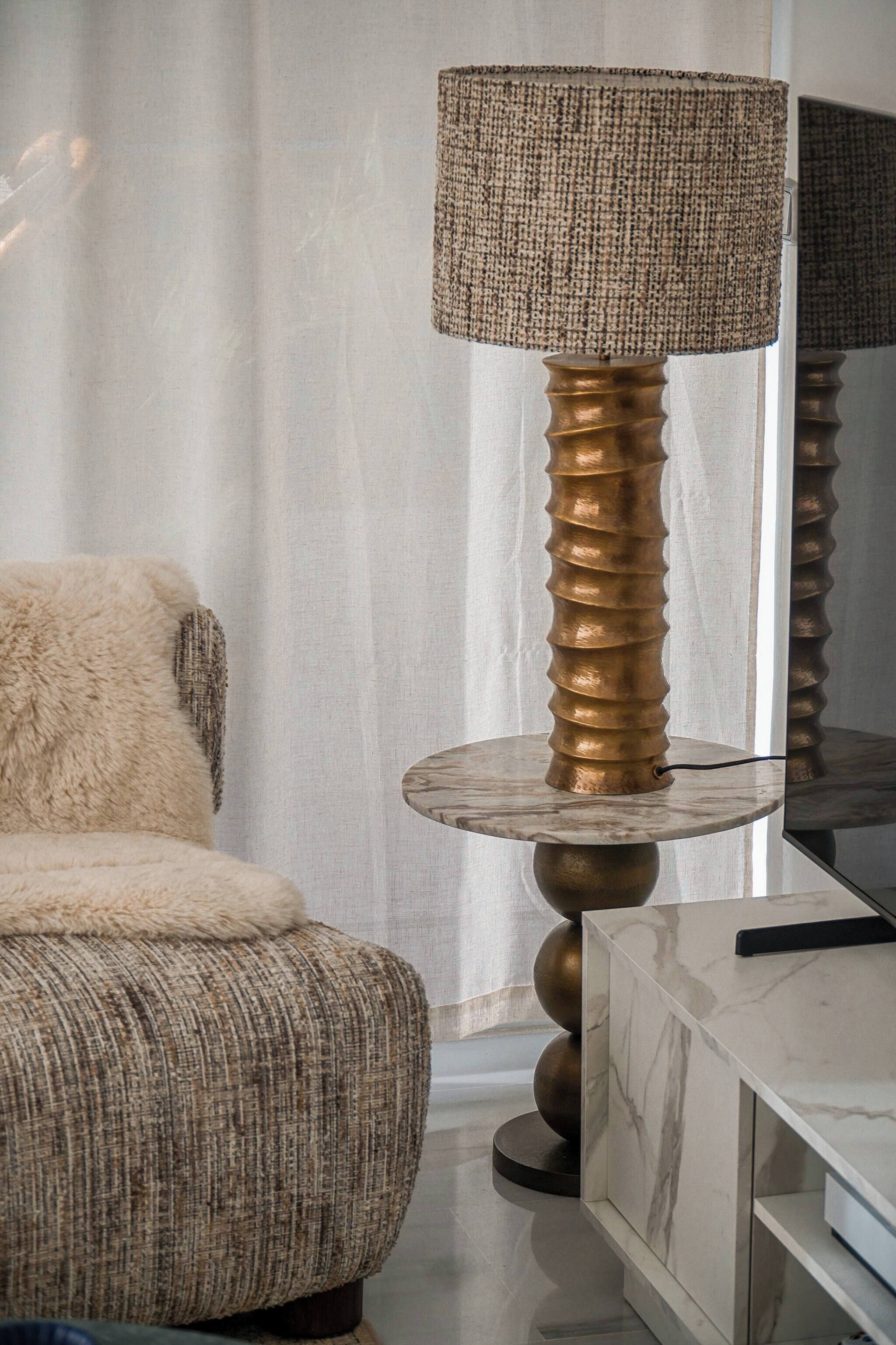 A modern room with a textured sofa, a round table with a lamp, and a marble cabinet.