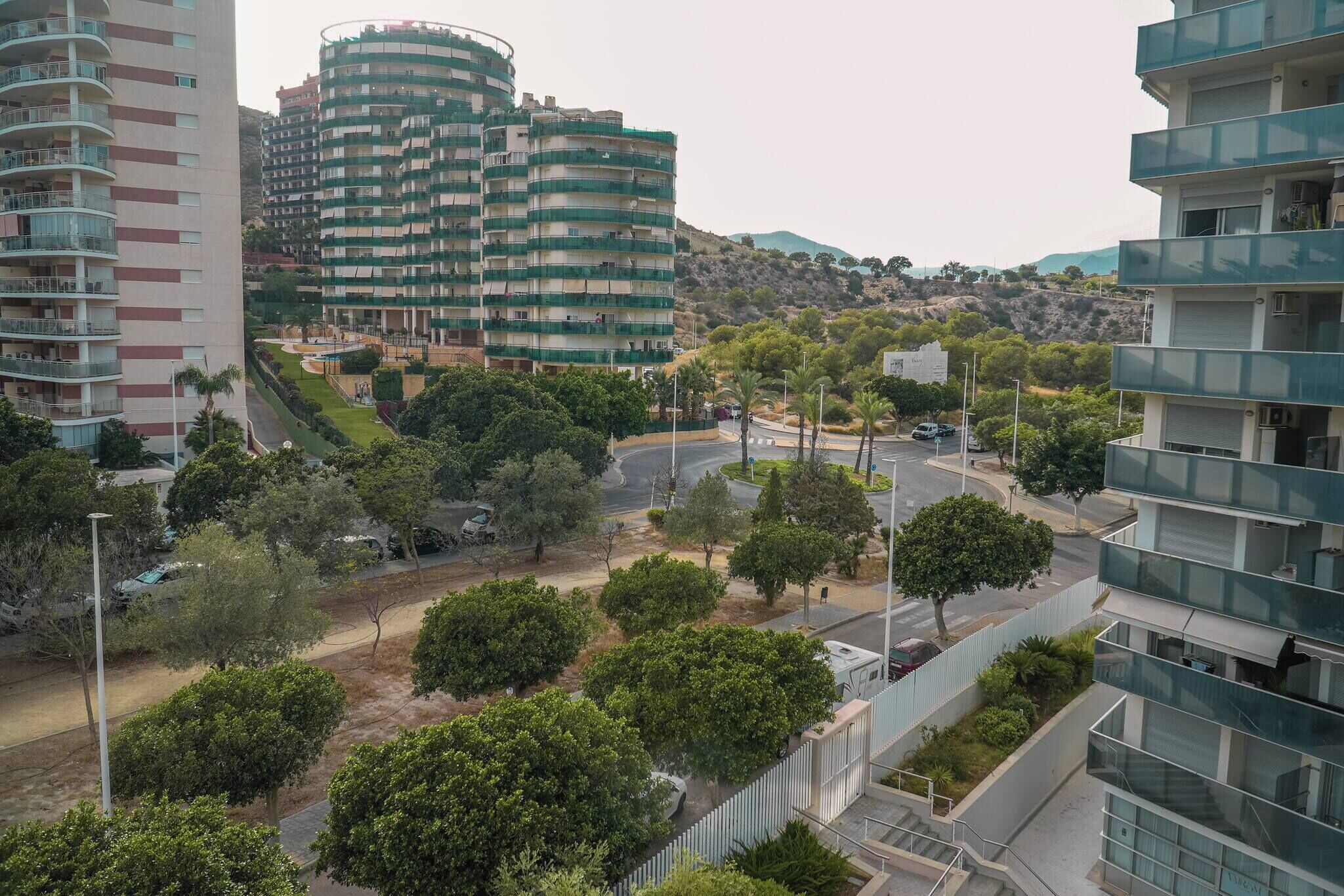 A residential area with multi-story buildings, a curved road, and greenery.
