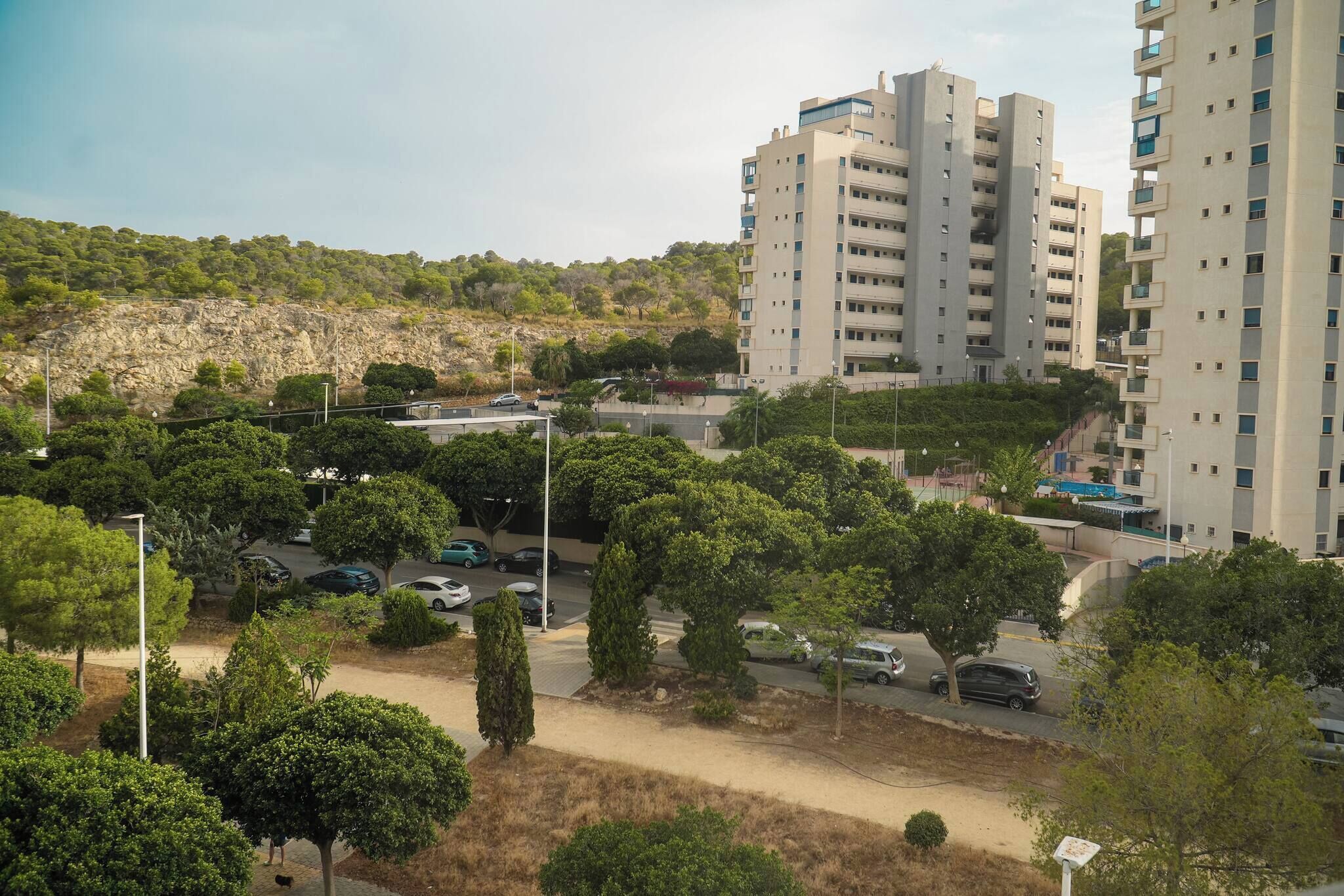 A residential area with multi-story buildings, a parking lot, and a hilly landscape in the background.