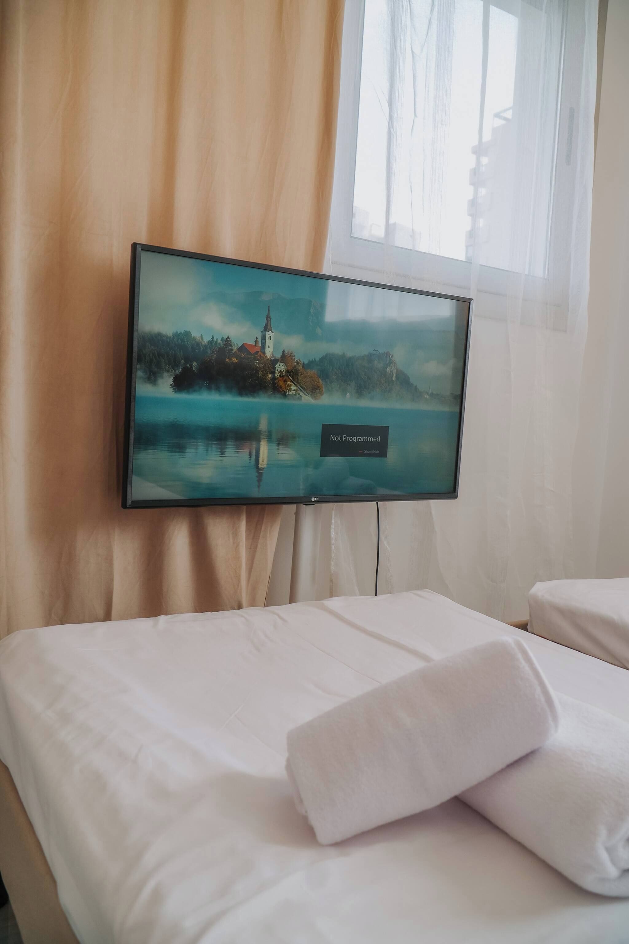 Una habitación de hotel con cama, televisión en la pared y ventana con cortinas.