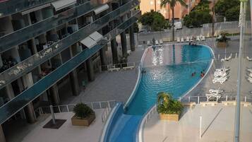 Una piscina de diseño curvo, rodeada de un sendero pavimentado y sillas de descanso.