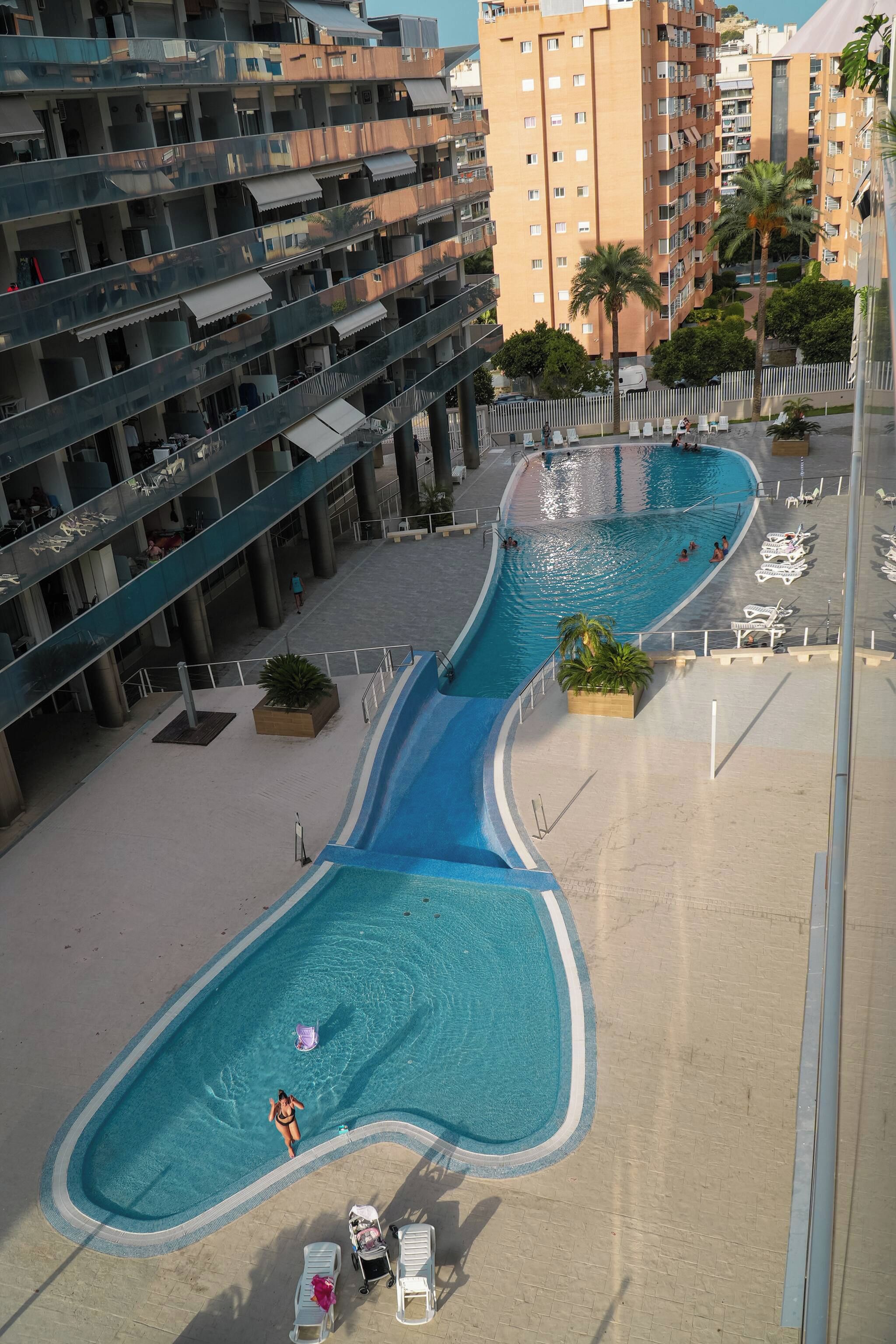 A swimming pool with a curved design, surrounded by a paved walkway and lounge chairs.