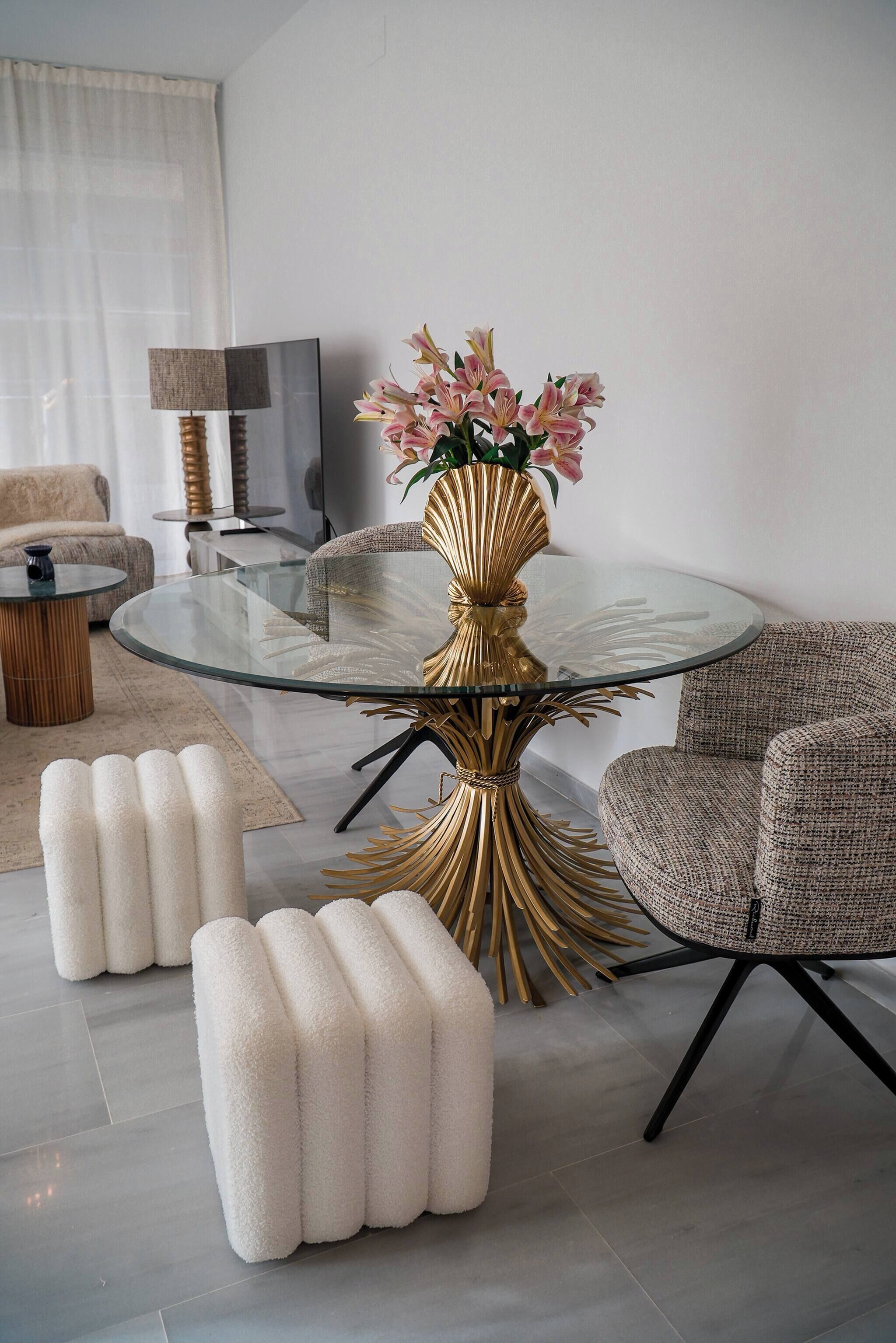 A modern living room with a glass coffee table, a gold decorative base, and a floral arrangement.
