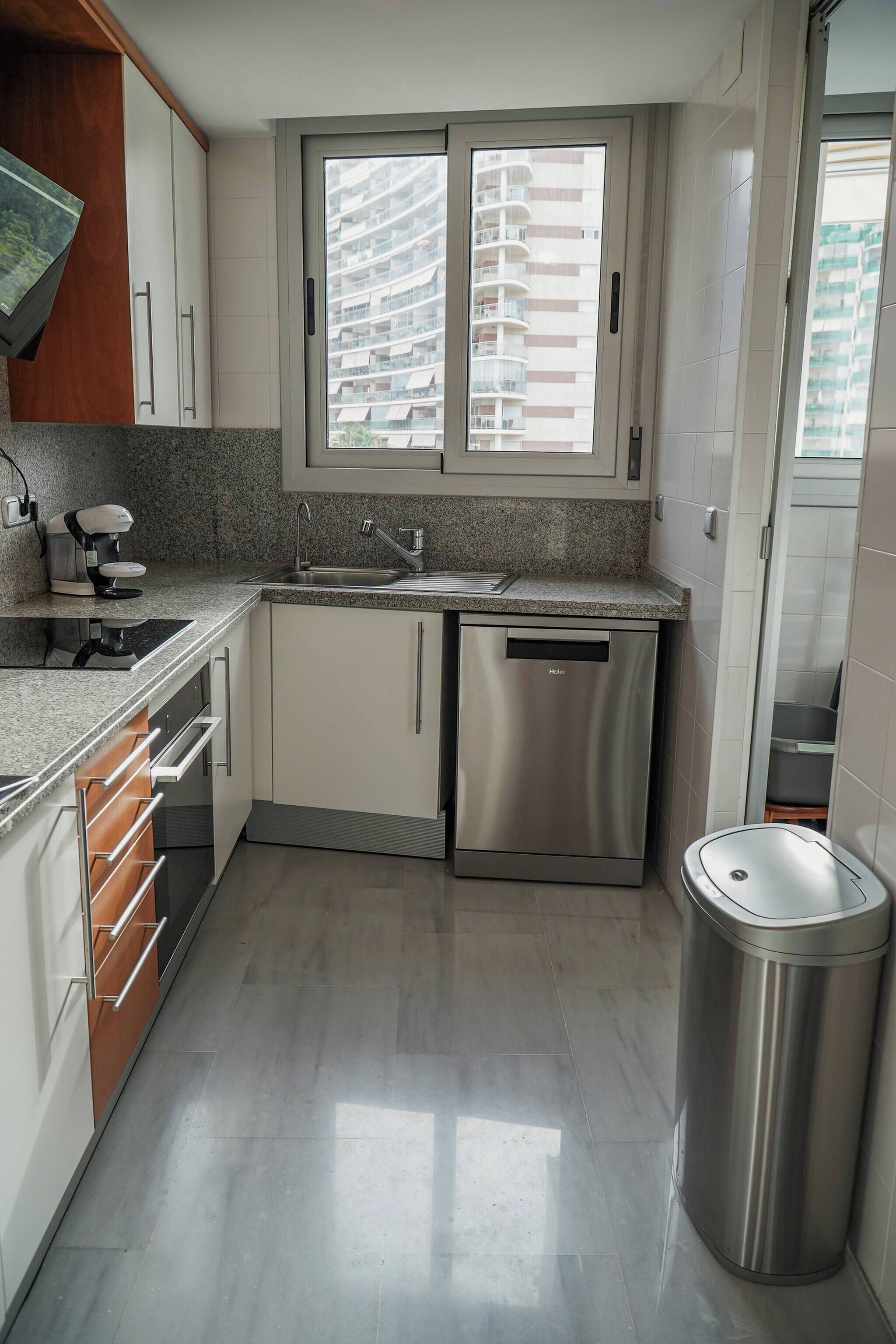 Una cocina moderna con lavavajillas integrado, cafetera y cubo de basura.