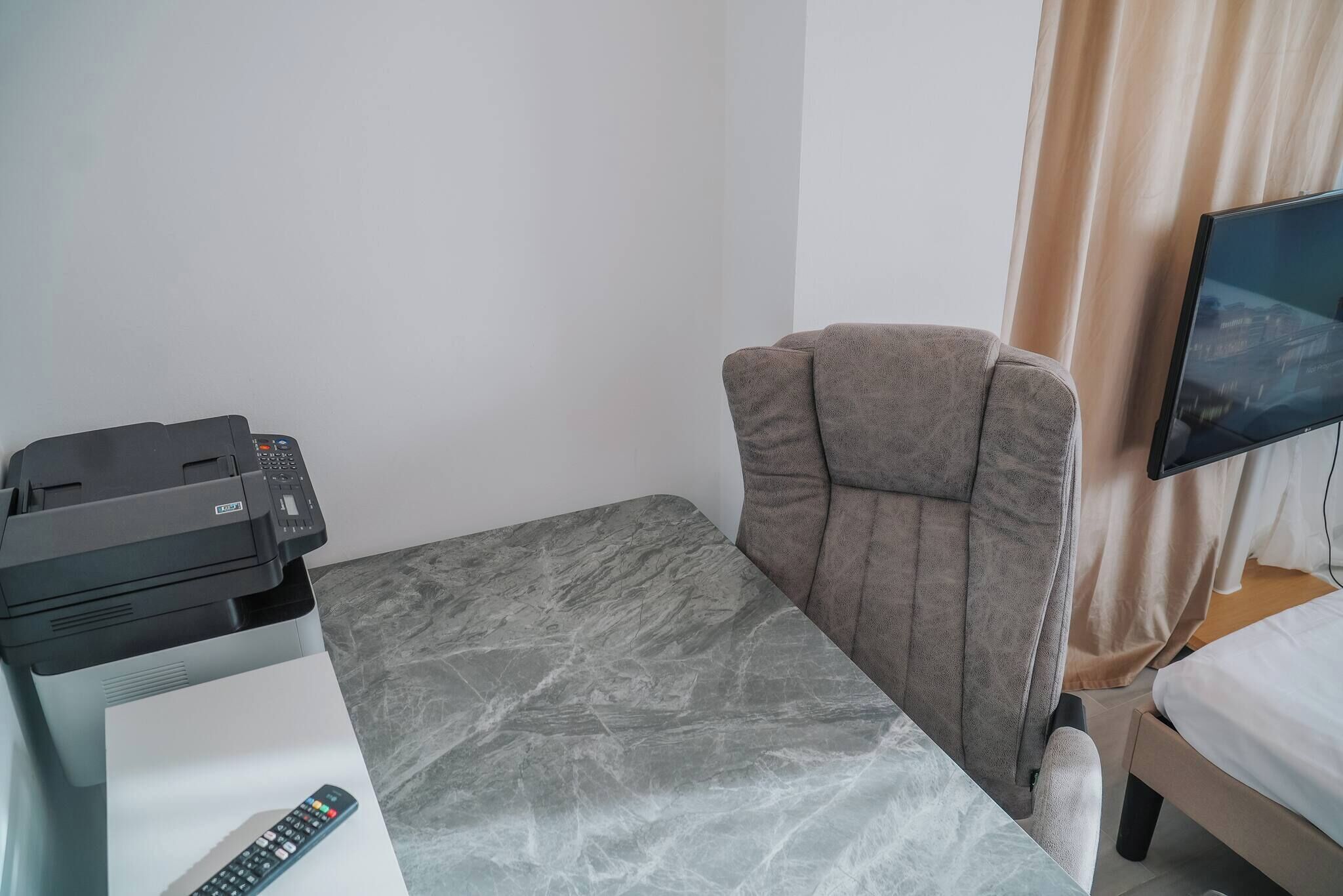 Habitación de hotel con cama, escritorio con impresora, silla, televisor y ventana con cortinas.