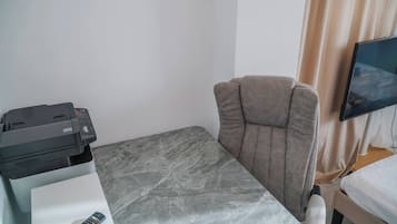 Habitación de hotel con cama, escritorio con impresora, silla, televisor y ventana con cortinas.