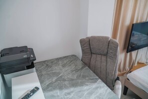 Habitació d'hotel amb llit, escriptori amb una impressora, cadira, televisió i finestra amb cortines.