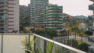 Un balcón con plantas en macetas, con vistas a una zona residencial con edificios de varios pisos y un paisaje montañoso.
