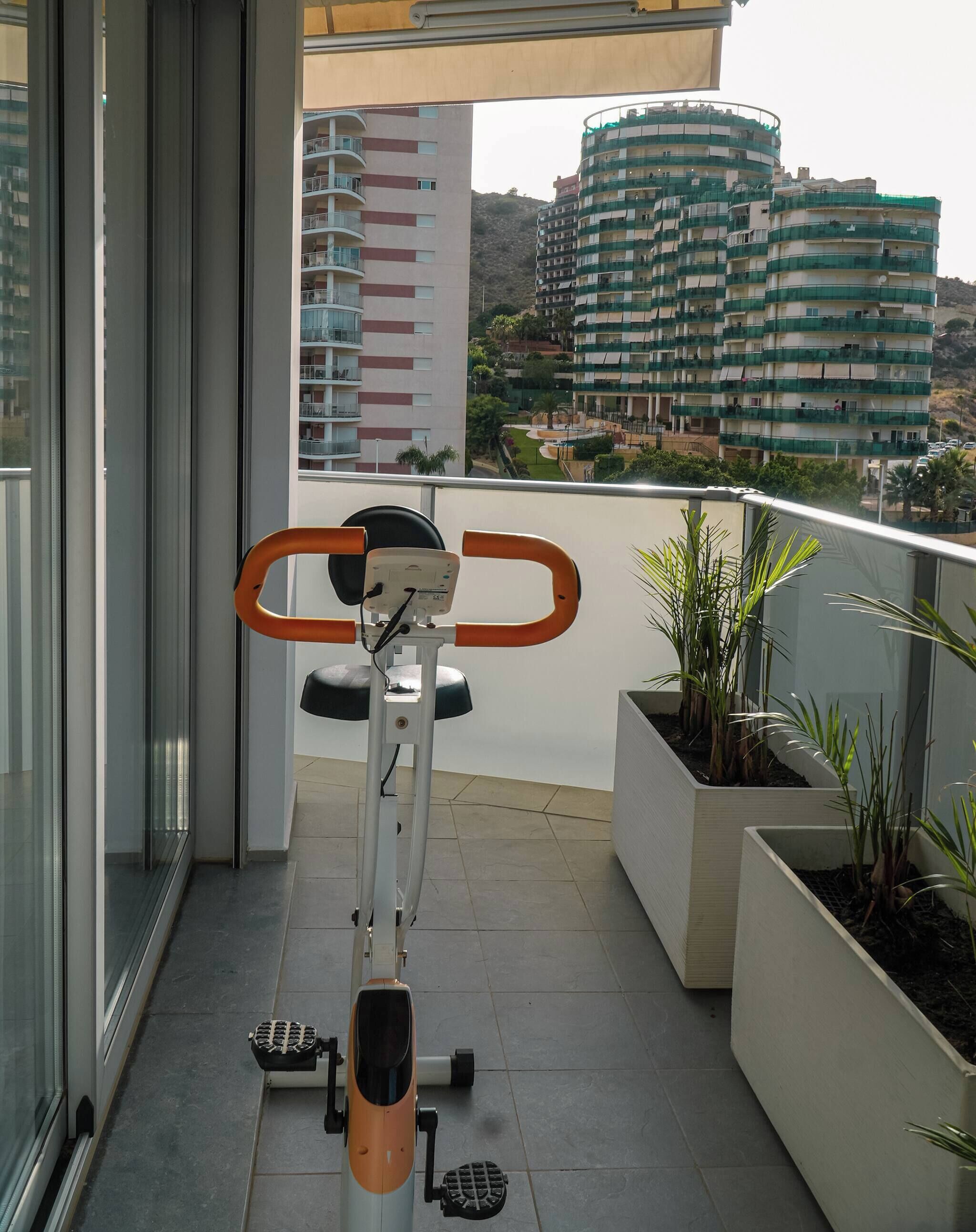 A balcony with an exercise bike, potted plants, and a view of residential buildings.