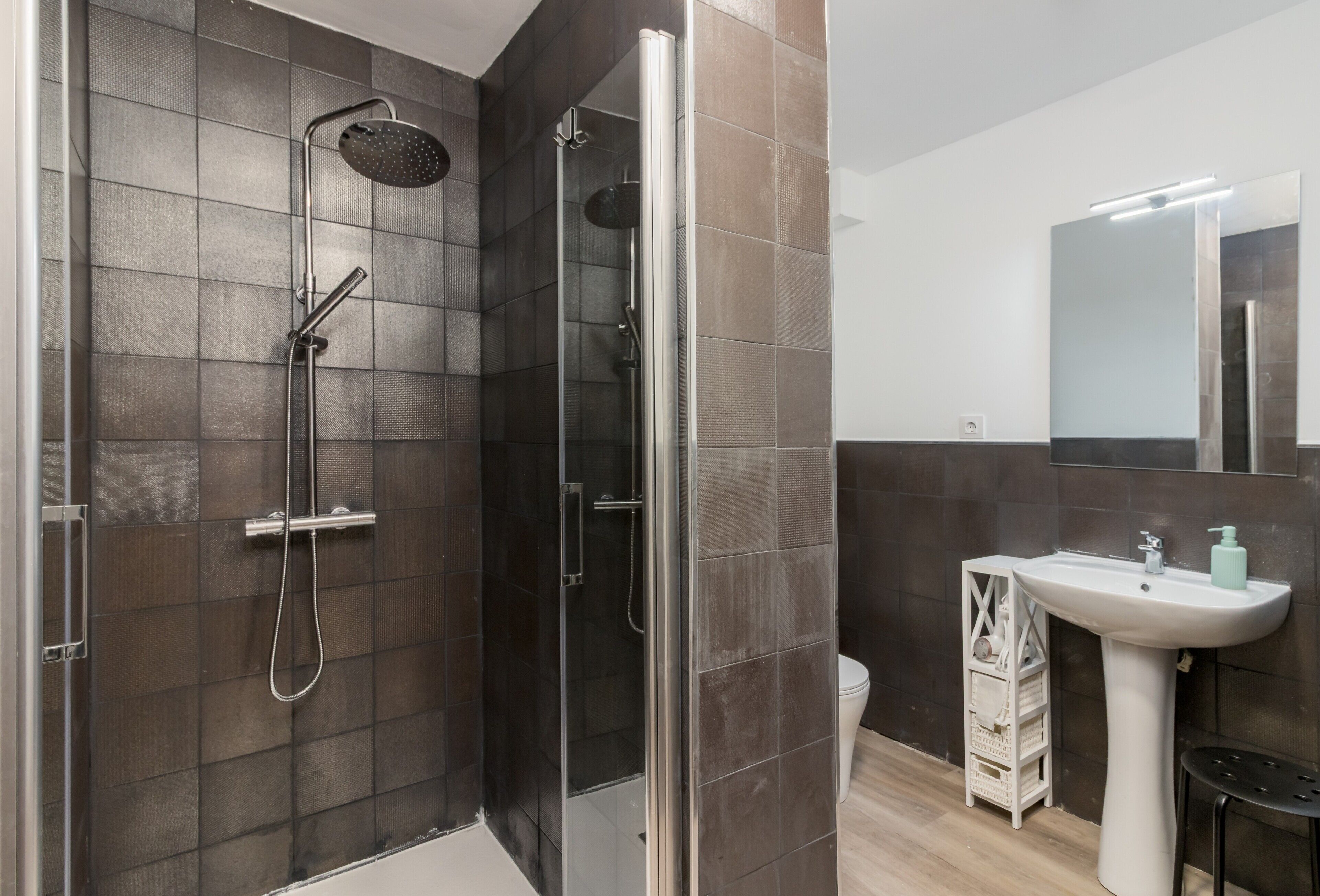 A modern bathroom with a glass-enclosed shower, a white sink, and a mirror above it.