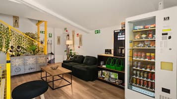Een modern interieur met een bank, een salontafel, een automaat en een trap met beplanting.