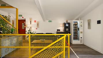 A hotel lobby with a yellow safety barrier, a vending machine, and a staircase with a red door.