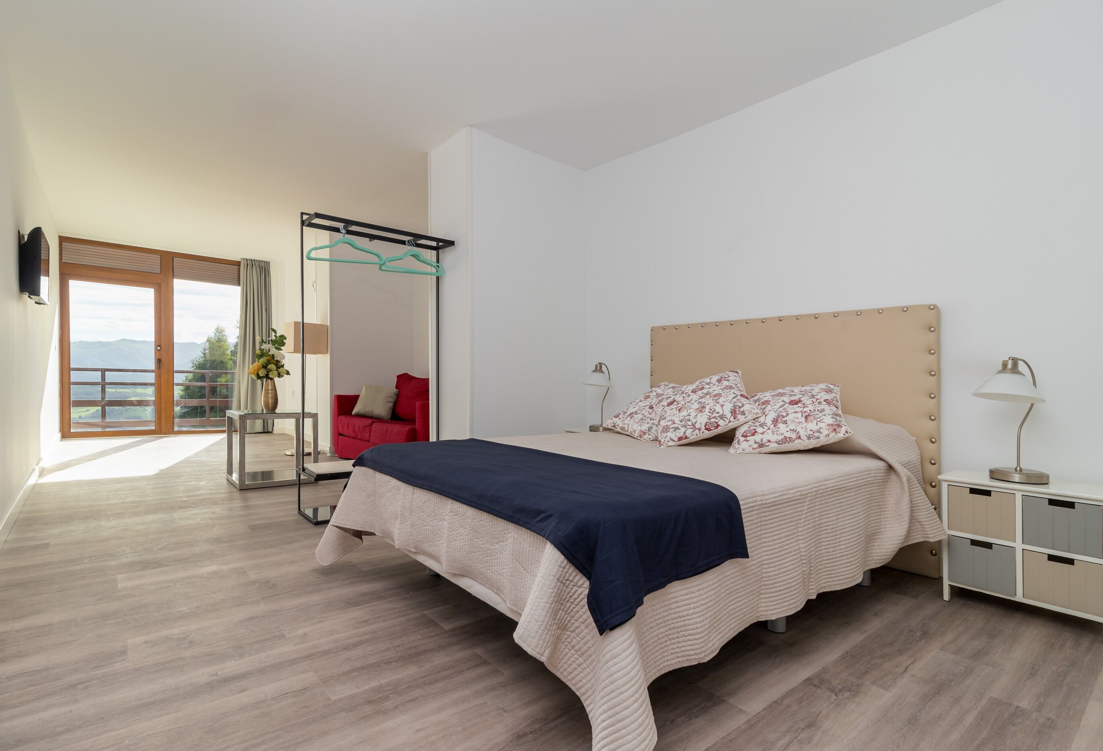 Un dormitorio con cama, una silla roja, un perchero y vistas al exterior.