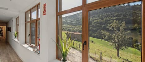 A corridor with large windows offering a view of a rural landscape.