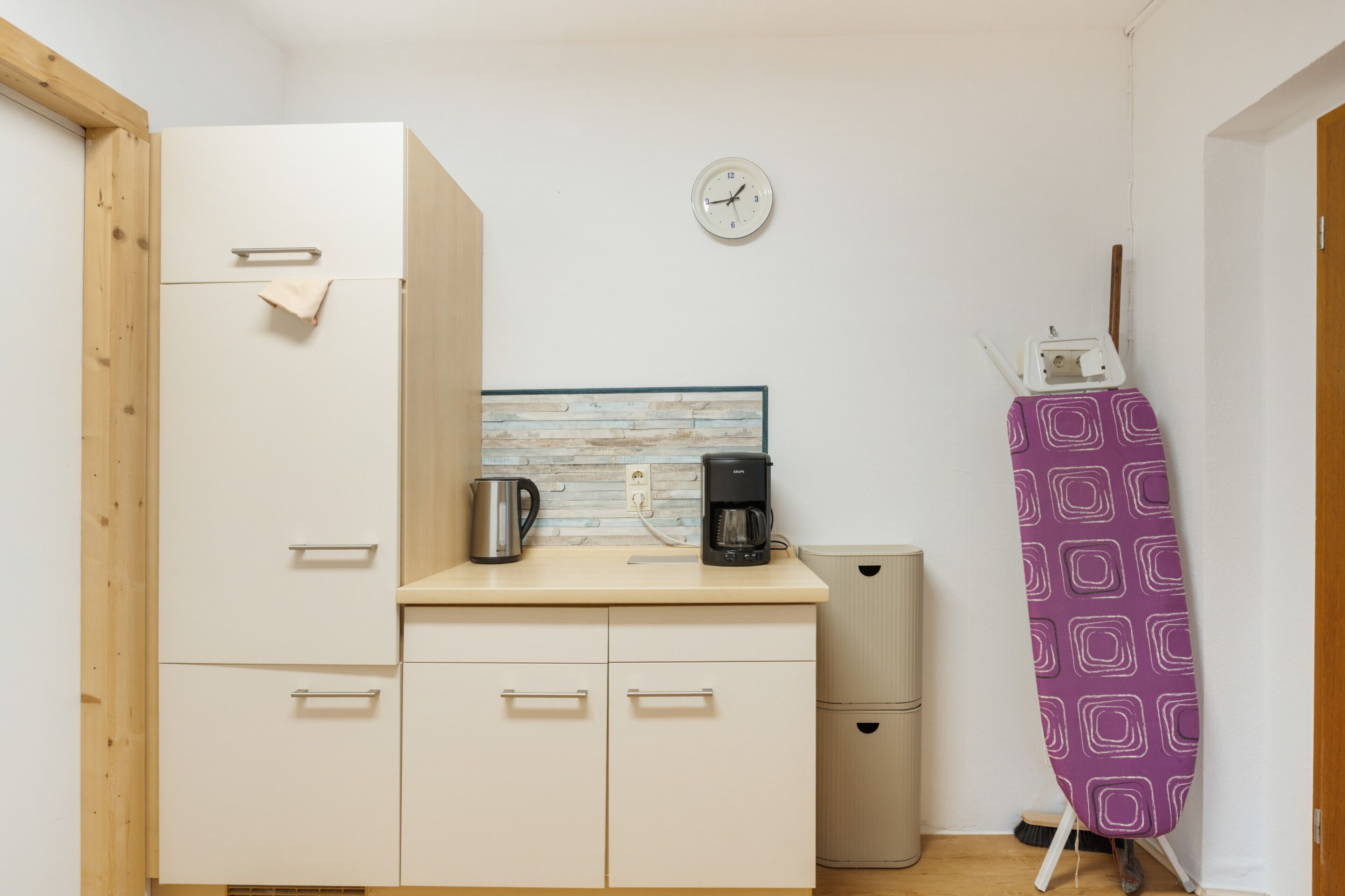 A compact kitchenette with a coffee maker, a kettle, and a clock on the wall.